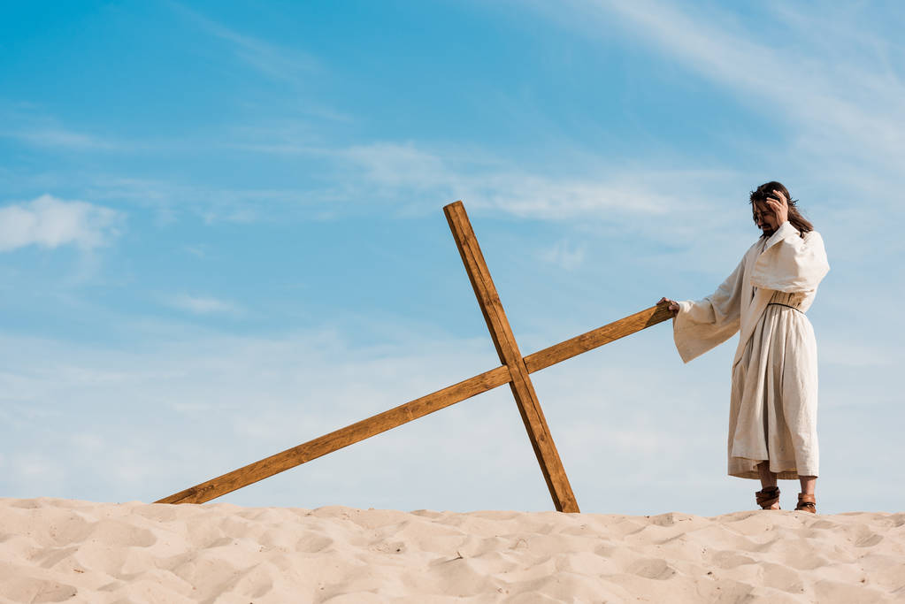 Szakállas férfi közel áll a fából készült kereszt a sivatagban homok  - Fotó, kép