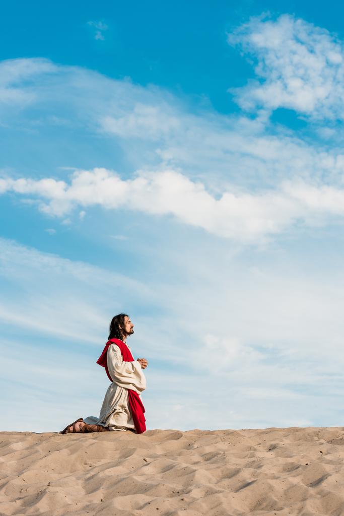 άνθρωπος προσεύχεται στα γόνατα με σφικτά χέρια στην έρημο με κυματιστή άμμο - Φωτογραφία, εικόνα