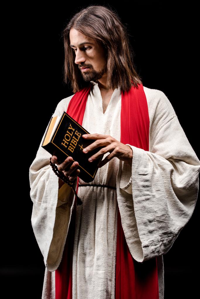 religieuze man in Jezus gewaad houden Heilige Bijbel geïsoleerd op zwart  - Foto, afbeelding