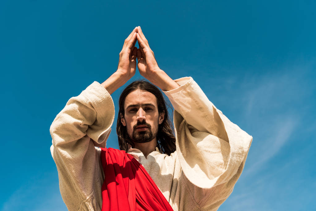 vista angolo basso di Gesù con la preghiera e guardando la fotocamera contro il cielo blu
  - Foto, immagini