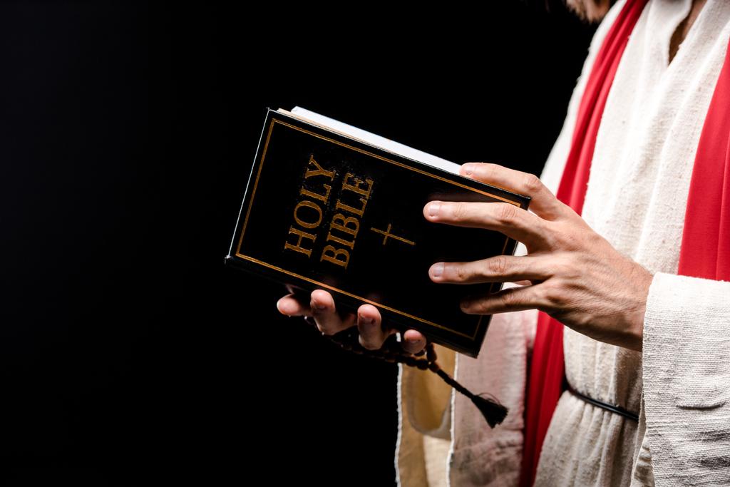 vista recortada del hombre sosteniendo el libro con letras sagradas de la Biblia aisladas en negro
  - Foto, imagen