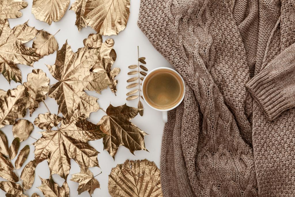 白い背景にニットブラウンのセーター、コーヒーと黄金の葉のトップビュー - 写真・画像
