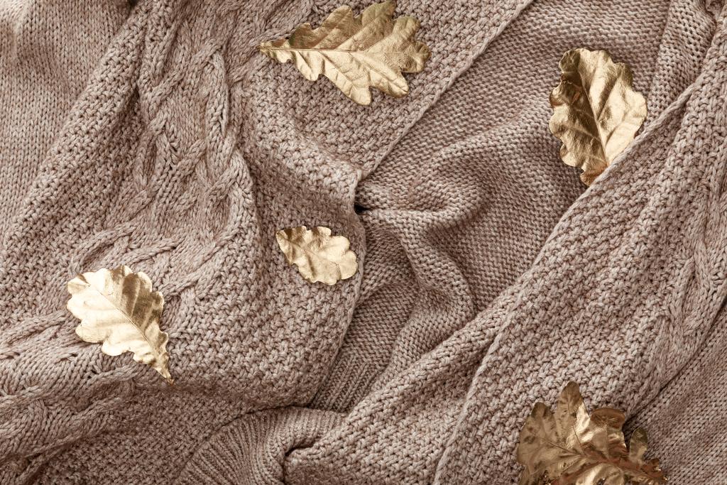 Top uitzicht van gebreide bruine trui met gouden geschilderde bladeren - Foto, afbeelding