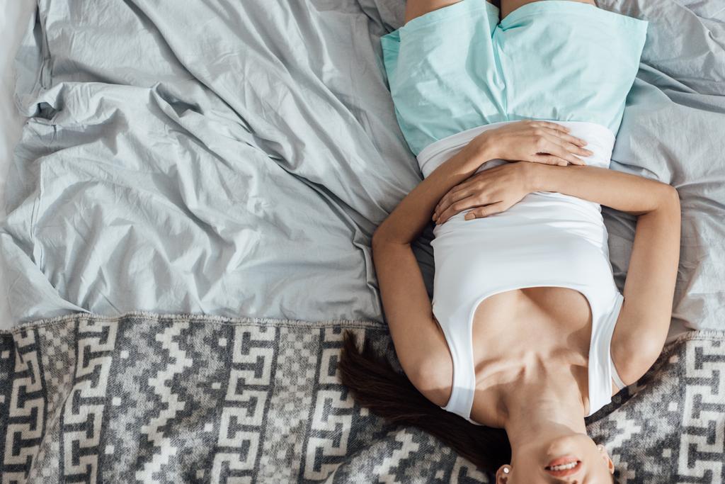 vista parcial de la mujer joven acostada en la cama y tocando el vientre
 - Foto, Imagen