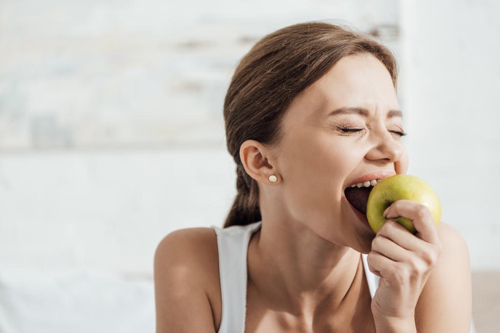 привлекательная молодая женщина ест зеленое яблоко с закрытыми глазами
 - Фото, изображение