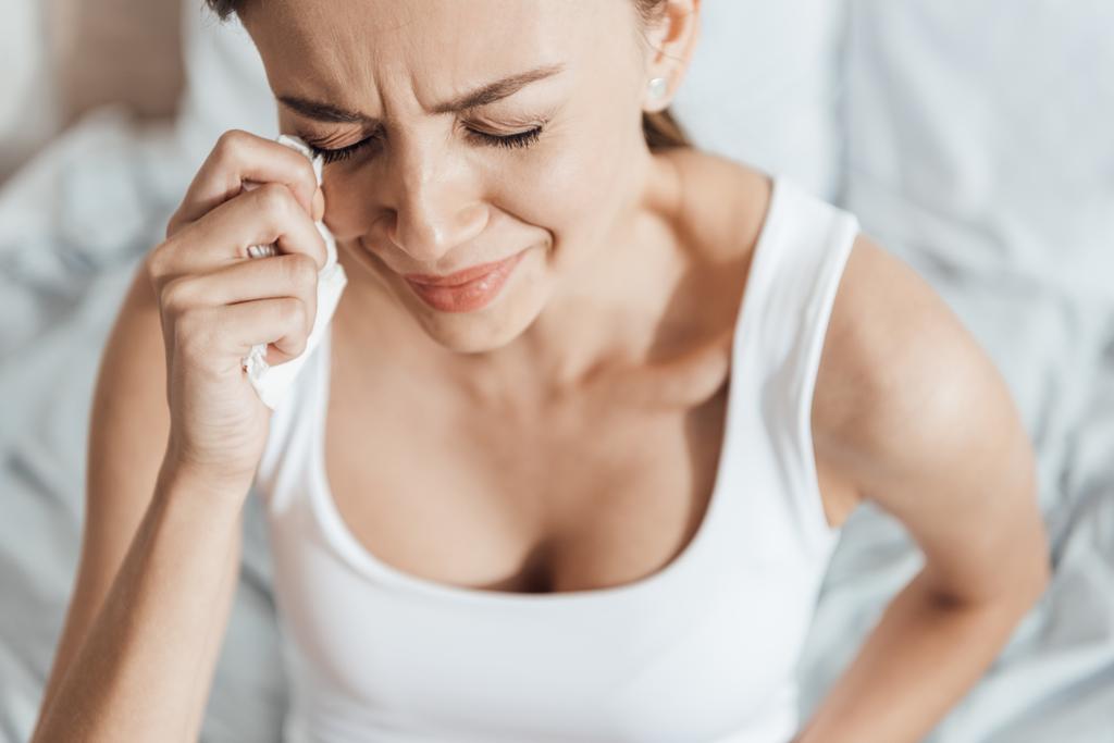 напряженная молодая женщина плачет и вытирает слезы салфеткой
 - Фото, изображение