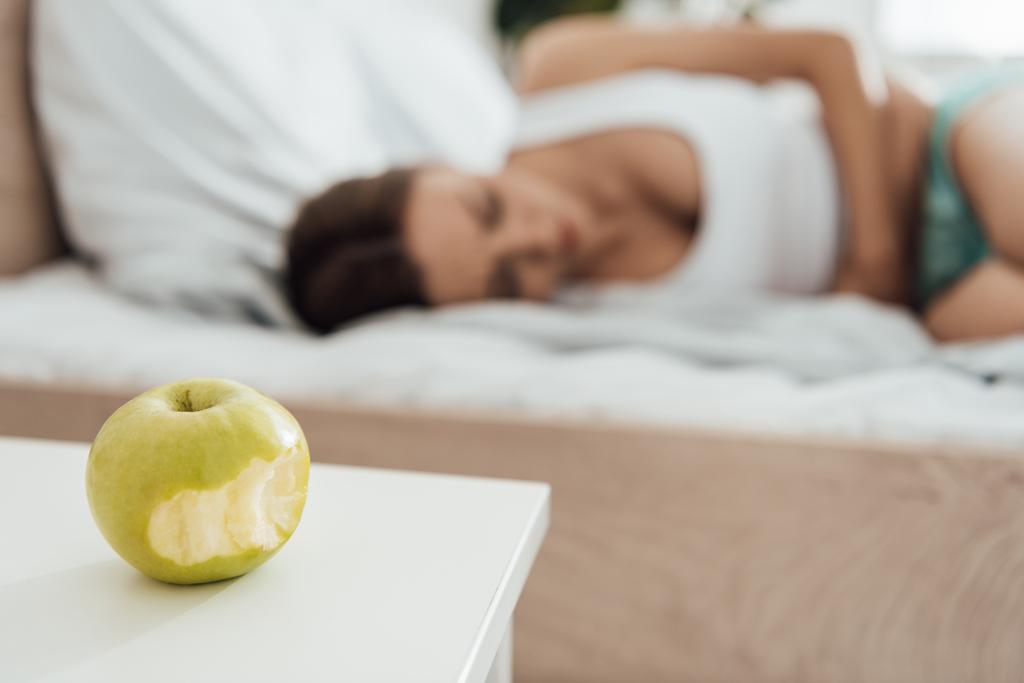 селективный фокус страдающей женщины, касающейся живота и зеленого яблока на переднем плане
 - Фото, изображение