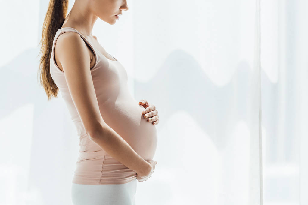 Обрізаний вид вагітної жінки, що торкається живота вдома
 - Фото, зображення