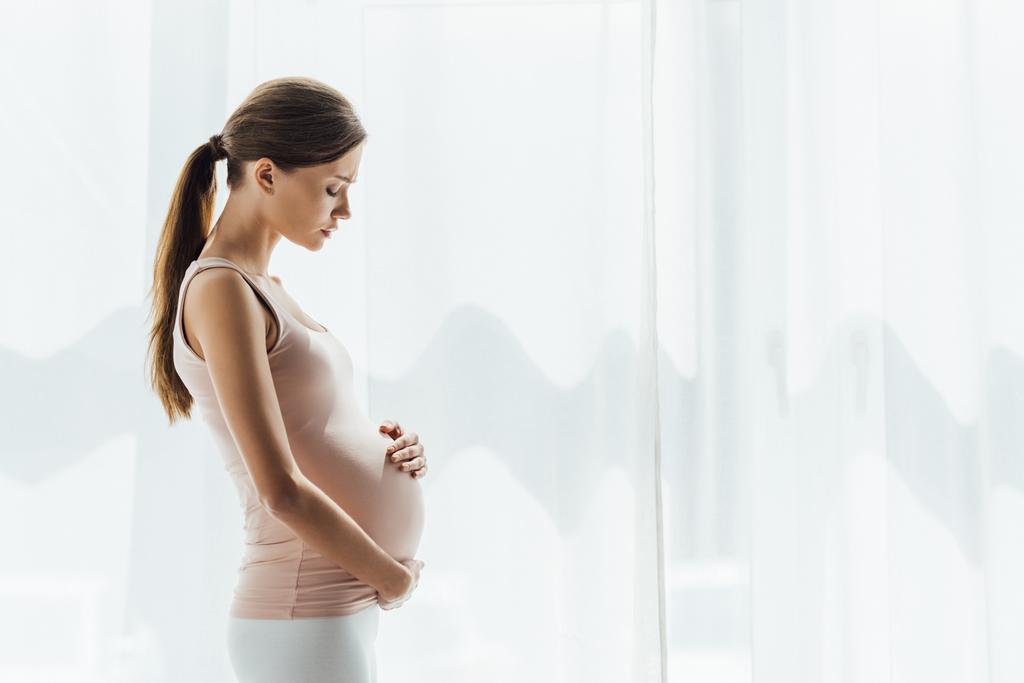 Seitenansicht einer schwangeren Frau, die Bauch mit geschlossenen Augen berührt - Foto, Bild