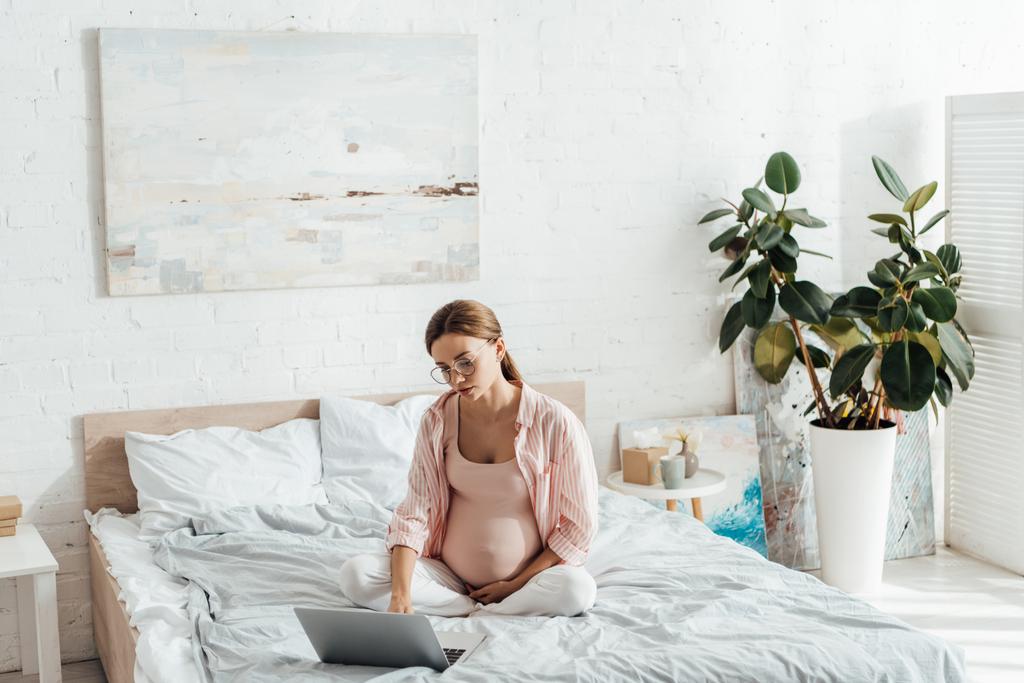femme enceinte dans des lunettes assis sur le lit et à l'aide d'un ordinateur portable
 - Photo, image