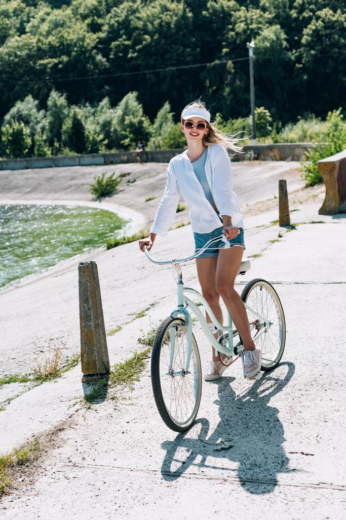 夏に川の近くで自転車に乗るブロンドの女の子 - 写真・画像