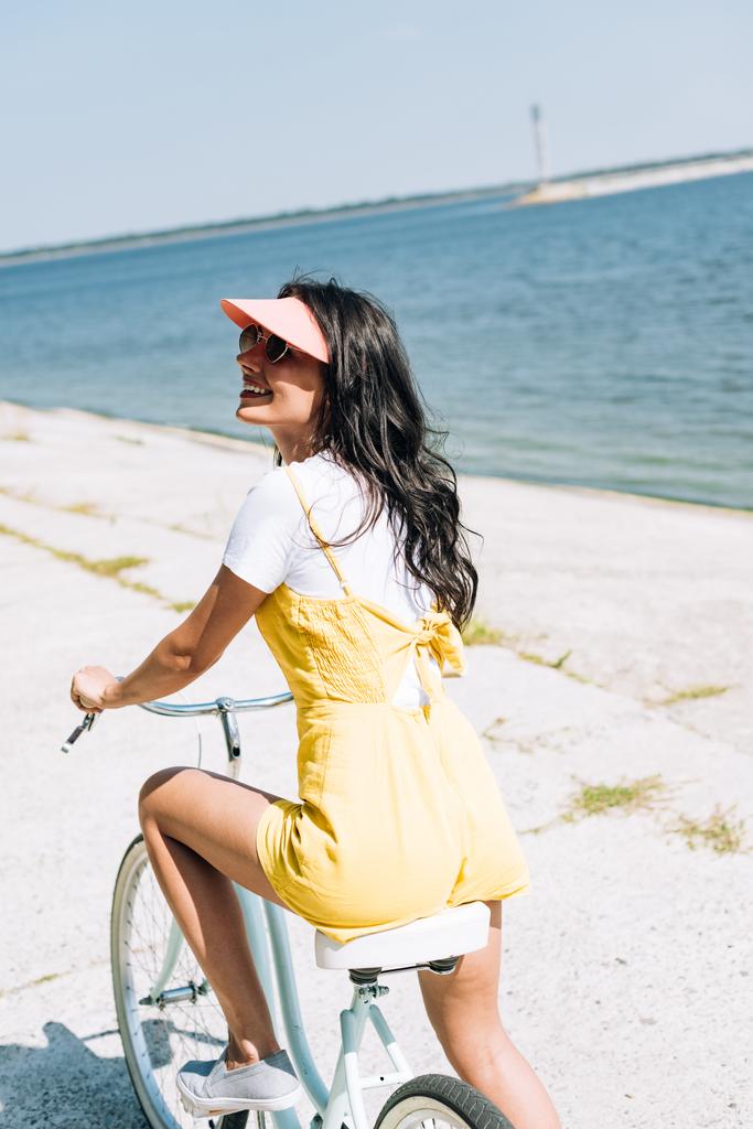 happy brunette girl riding bike near river in summer - Photo, Image