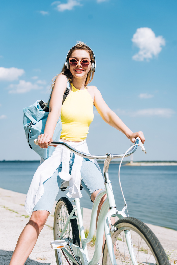menina com mochila de bicicleta e ouvir música em fones de ouvido perto do rio
 - Foto, Imagem