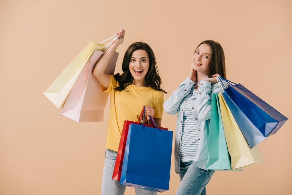 attractive and smiling friends holding shopping bags isolated on beige - Photo, Image