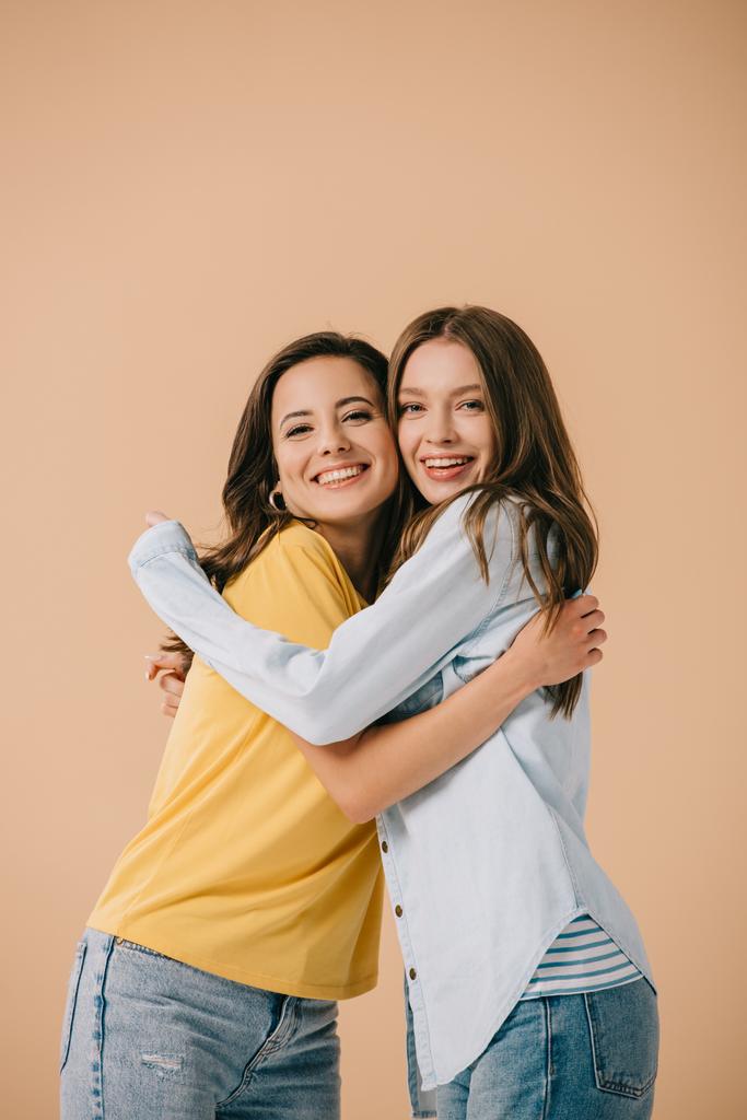 attractive and smiling friends hugging and looking at camera isolated on beige - Photo, Image