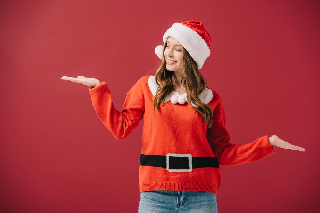 atraktivní žena v Santa klobouku a svetru s napřaženou rukou izolovanými na Rudém  - Fotografie, Obrázek