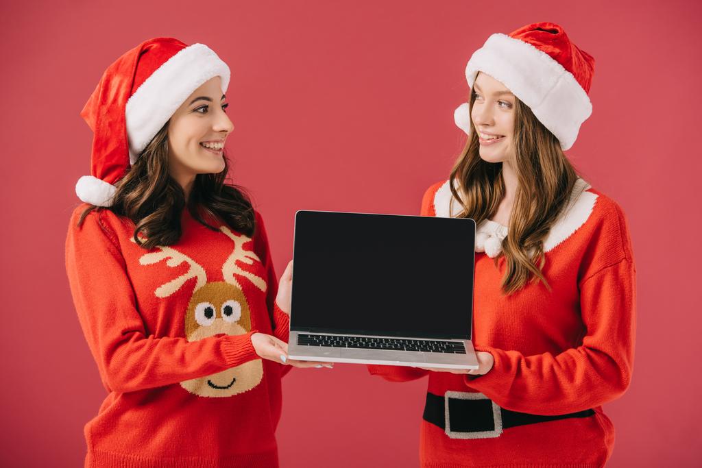 attrayant et souriant femmes en chandails et Père Noël tenant ordinateur portable isolé sur rouge
  - Photo, image