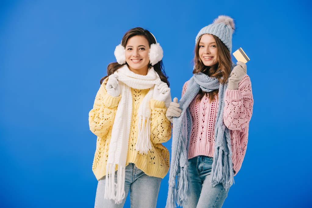 привабливі і усміхнені жінки в светрах і шарфах тримають кредитну картку ізольовані на синьому
 - Фото, зображення