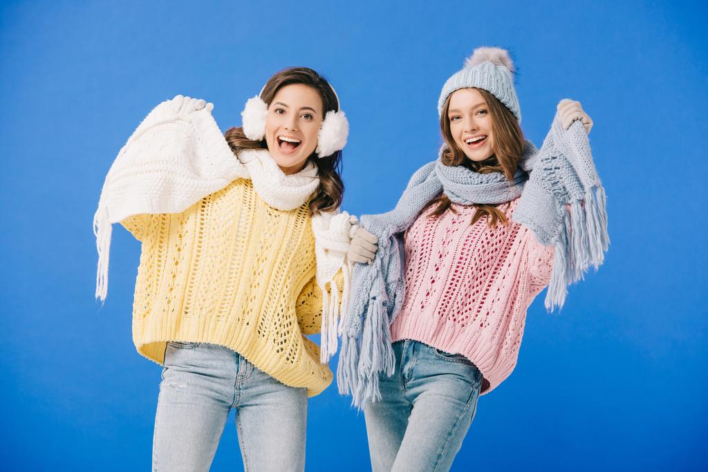 attractive and smiling women in sweaters and scarves looking at camera isolated on blue - Photo, Image