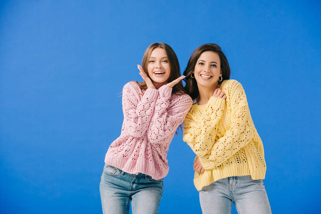 mujeres atractivas y sonrientes en suéteres mirando a la cámara aislada en azul
  - Foto, imagen