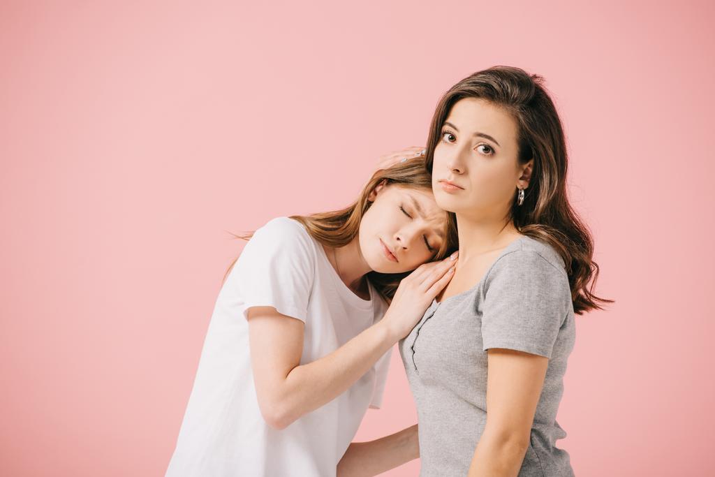 aantrekkelijke en trieste vrouwen in t-shirts knuffelen geïsoleerd op roze - Foto, afbeelding