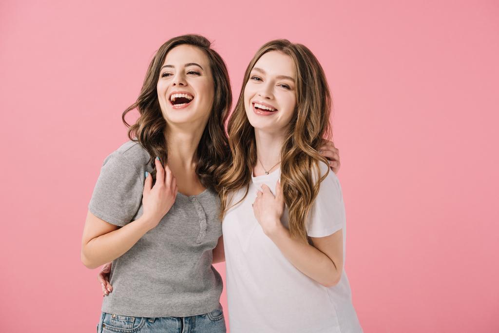 ελκυστικές και χαμογελαστές γυναίκες σε μπλουζάκια που κοιτάζουν την κάμερα απομονωμένη σε ροζ - Φωτογραφία, εικόνα