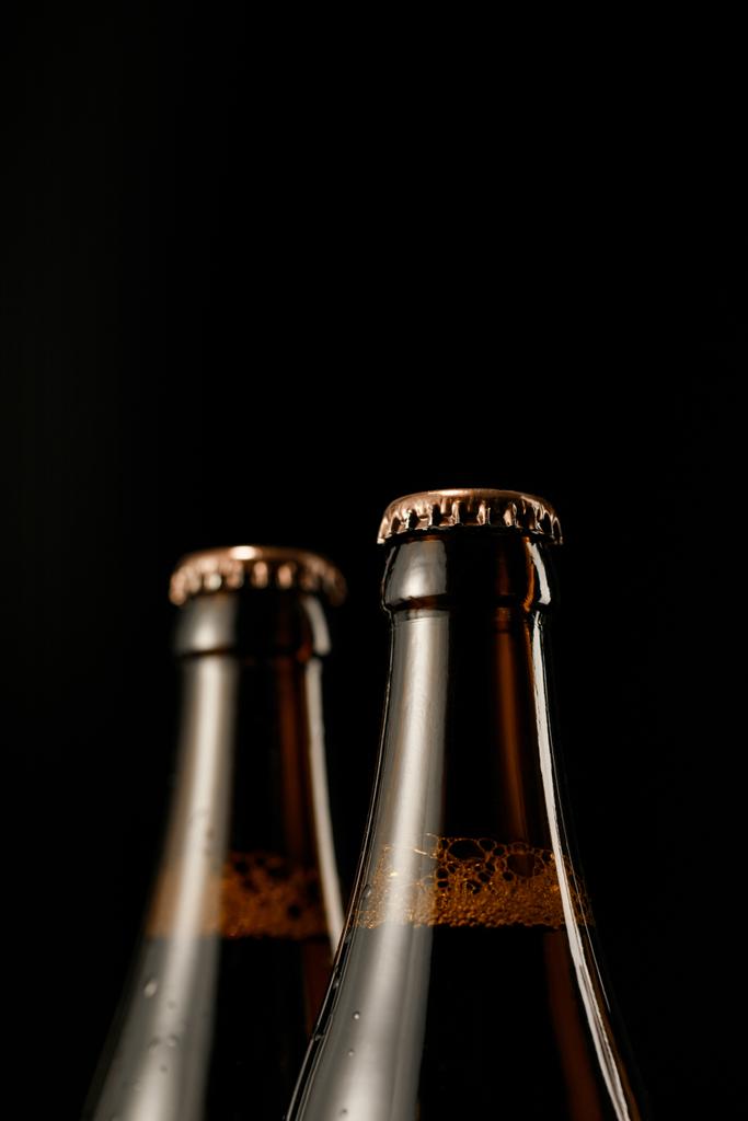 Κλείστε θέα από γυάλινες φιάλες μπύρας με καπάκια απομονωμένα σε μαύρο - Φωτογραφία, εικόνα