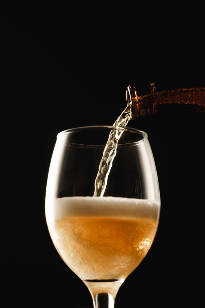 Χρυσή μπύρα που ρέει από το μπουκάλι σε γυαλί απομονώνεται σε μαύρο - Φωτογραφία, εικόνα