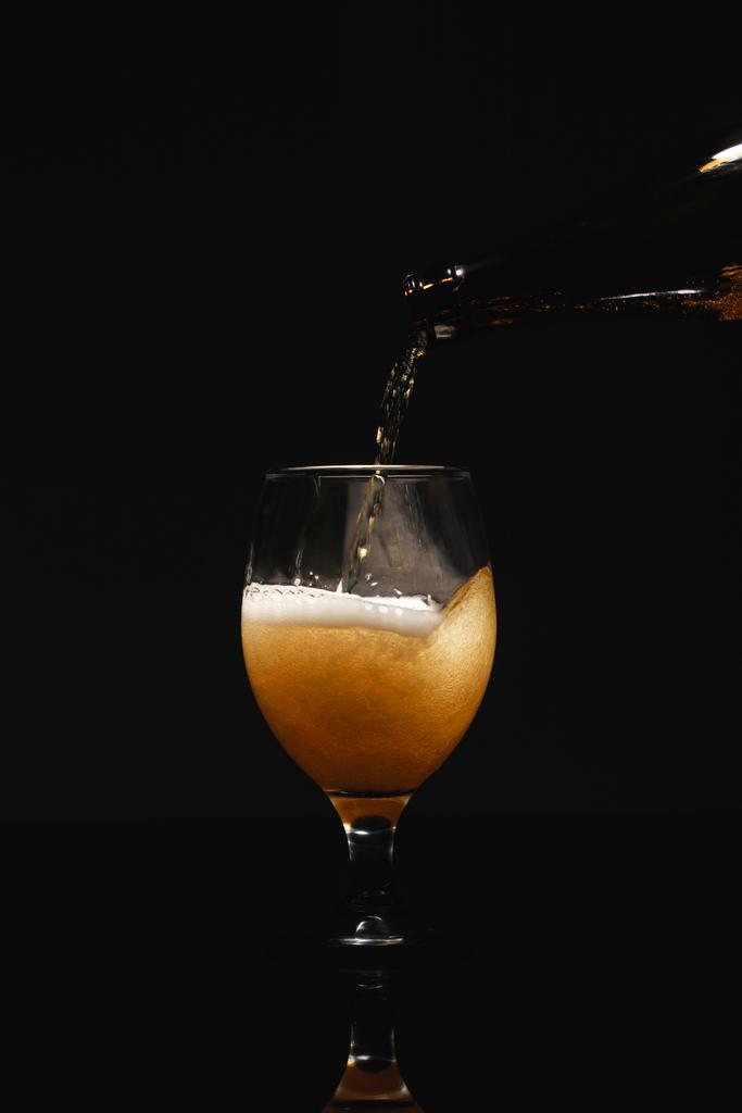 Bier fließt aus Flasche in Glas isoliert auf schwarz - Foto, Bild