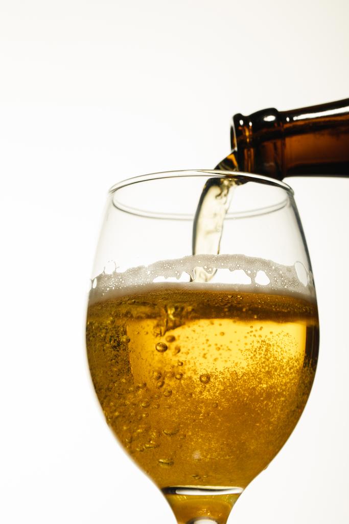 χαμηλή γωνιακή θέα της μπύρας που χύνεται από φιάλη σε γυαλί που απομονώνεται σε λευκό - Φωτογραφία, εικόνα