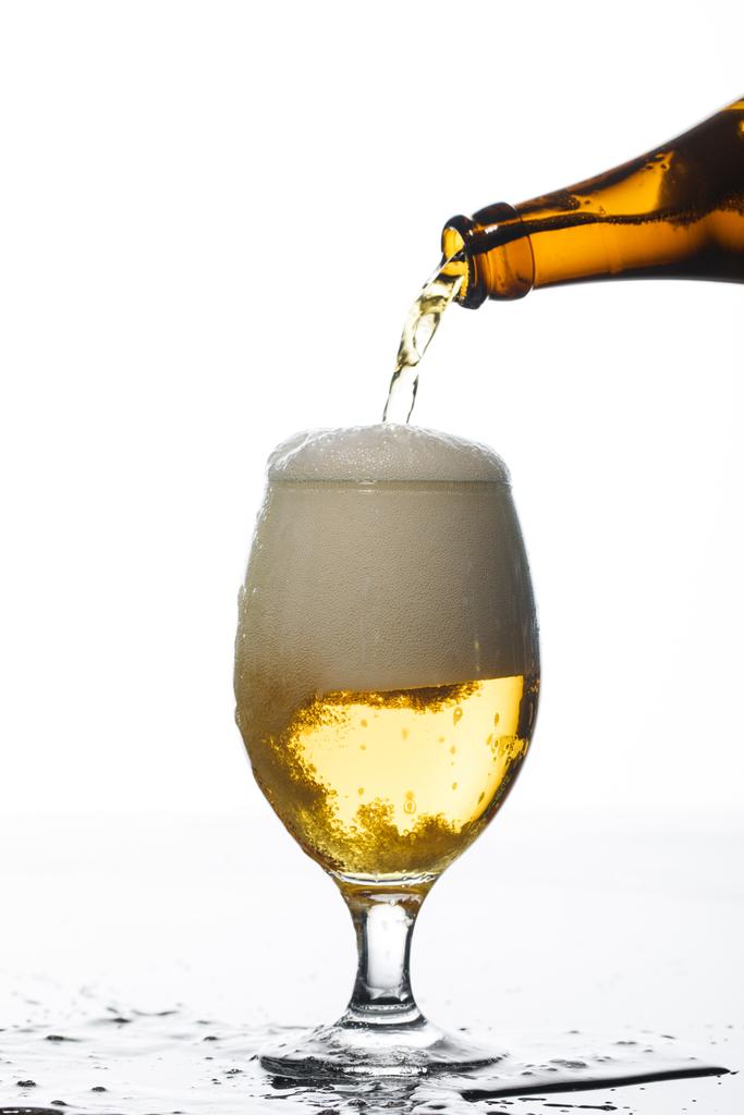 beer pouring from bottle into glass on surface with puddle isolated on white - Photo, Image