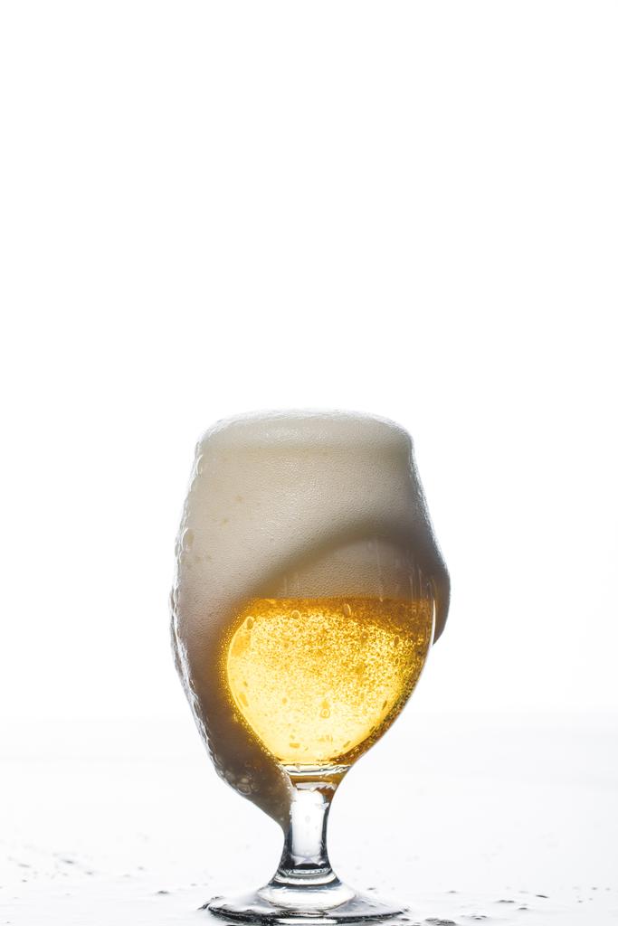υγρό ποτήρι μπύρας με αφρό που χύθηκε σε λευκό - Φωτογραφία, εικόνα