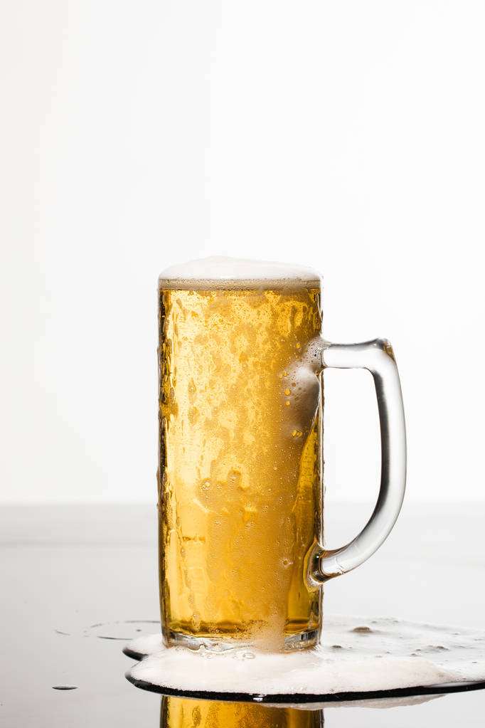 vaso húmedo de cerveza con espuma y charco derramado en la superficie aislada en blanco
 - Foto, imagen