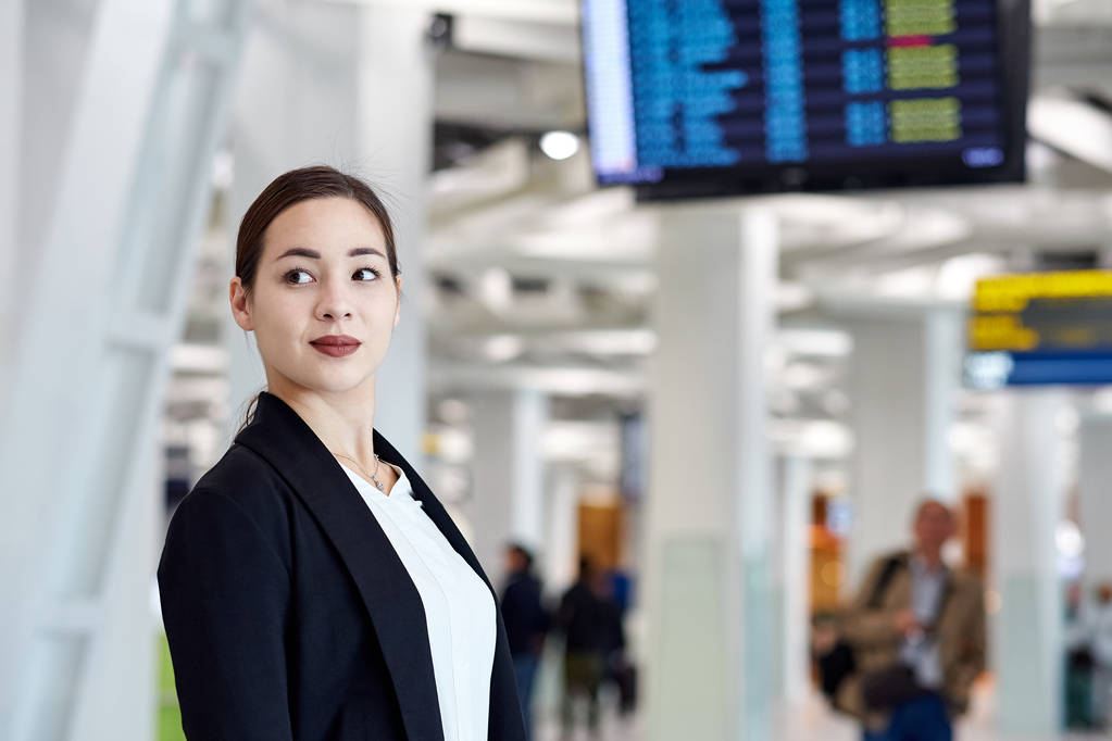 Joven mujer de negocios asiática en el aeropuerto con bolsa de carro, esperando la salida
 - Foto, Imagen