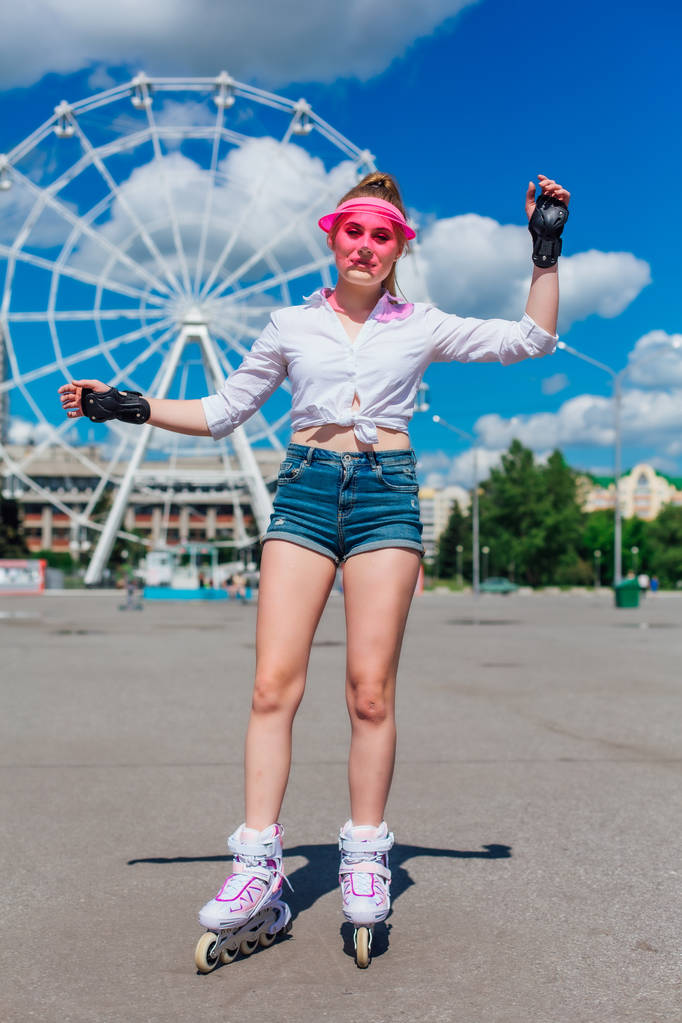 Portret emocjonalnej dziewczyny w różowym daszkiem i rękawice ochronne do rolek i skateboardingu jazda na rolkach na drodze. - Zdjęcie, obraz