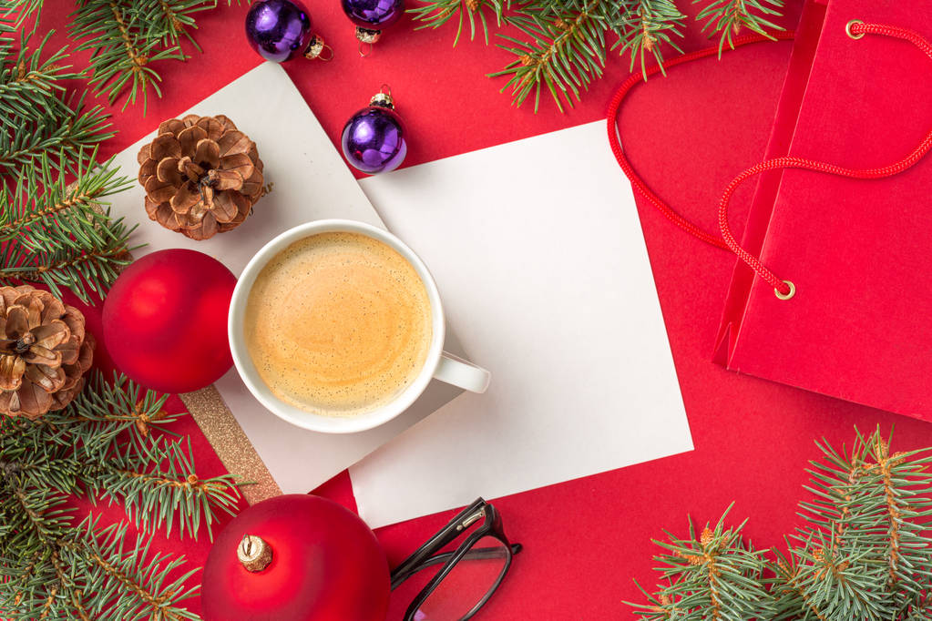 Kerstversiering met Kladblok, pen, bril en kopje koffie op rood werkblad bovenaanzicht - Foto, afbeelding