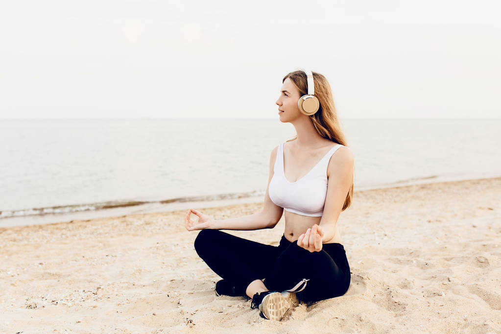 Young athletic girl, meditating outdoors at sea, and listening t - Photo, Image