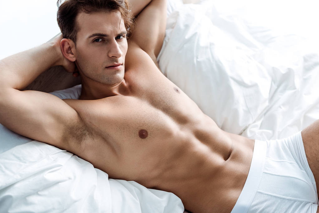 νέος σέξι άνθρωπος ξαπλωμένο στο κρεβάτι και κοιτάζοντας την κάμερα - Φωτογραφία, εικόνα
