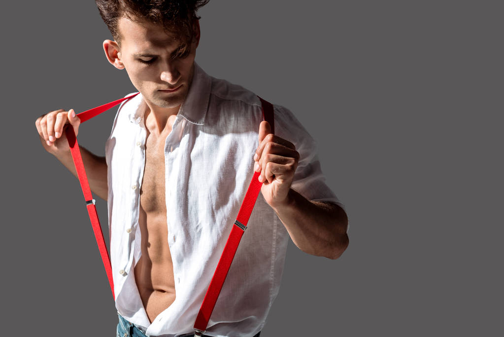 灰色に隔離された赤いサスペンダーに触れる白いシャツのハンサムな男  - 写真・画像
