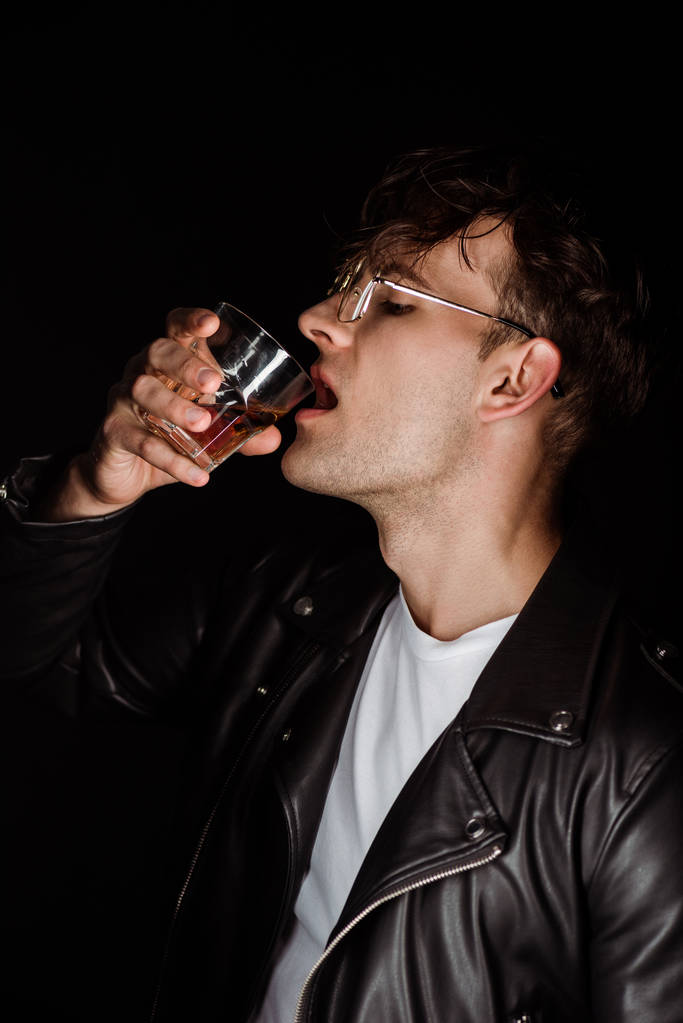 brutale man houdt glas en drinken van whiskey geïsoleerd op zwart  - Foto, afbeelding