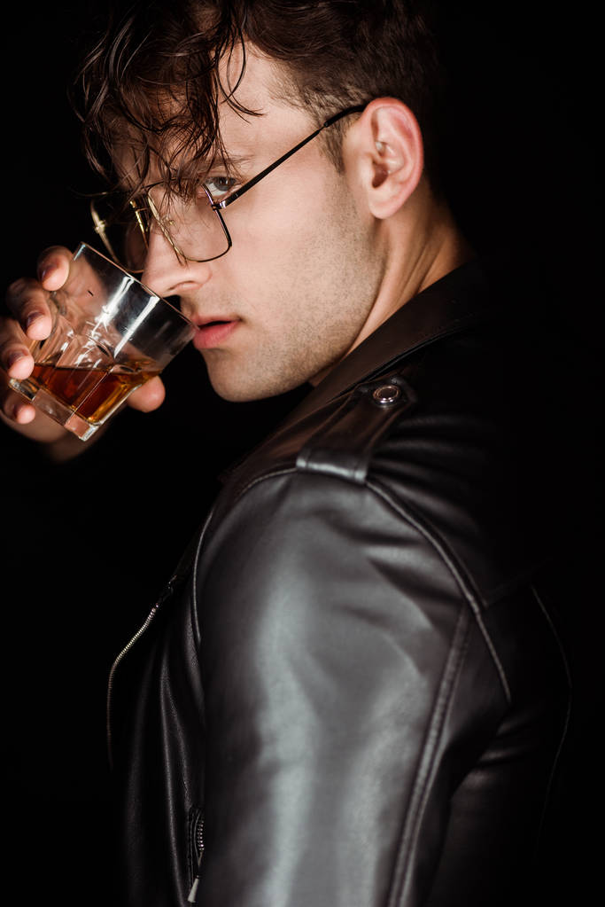 brutal man in eye glasses holding glass with whiskey isolated on black  - Photo, Image