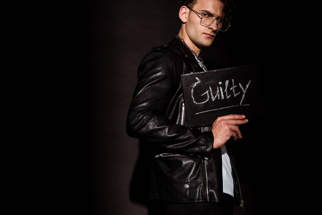 κομψός άνθρωπος σε γυαλιά κρατώντας κιμωλία σανίδα με ένοχη γραφή σε μαύρο   - Φωτογραφία, εικόνα
