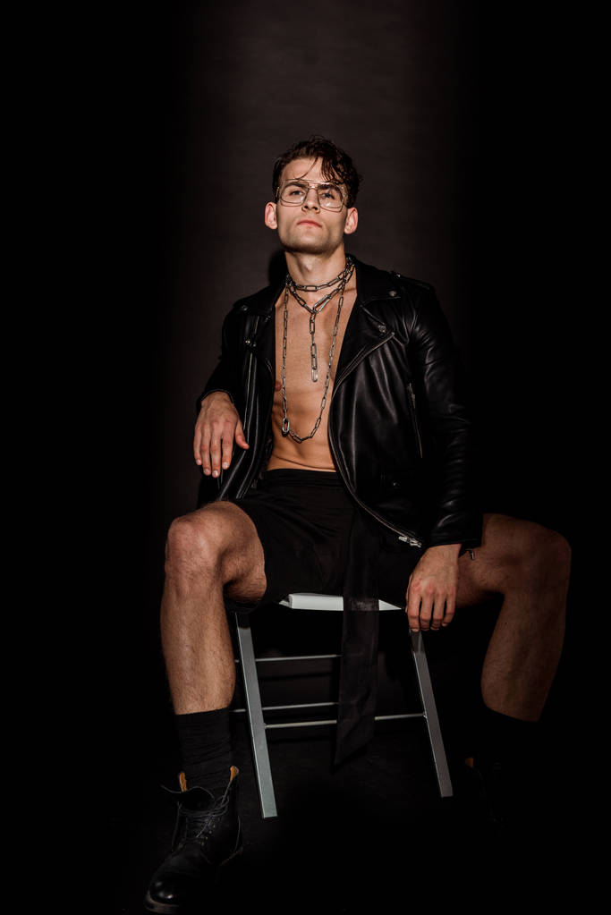 жестокий молодой человек в кожаной куртке сидит на черном
  - Фото, изображение