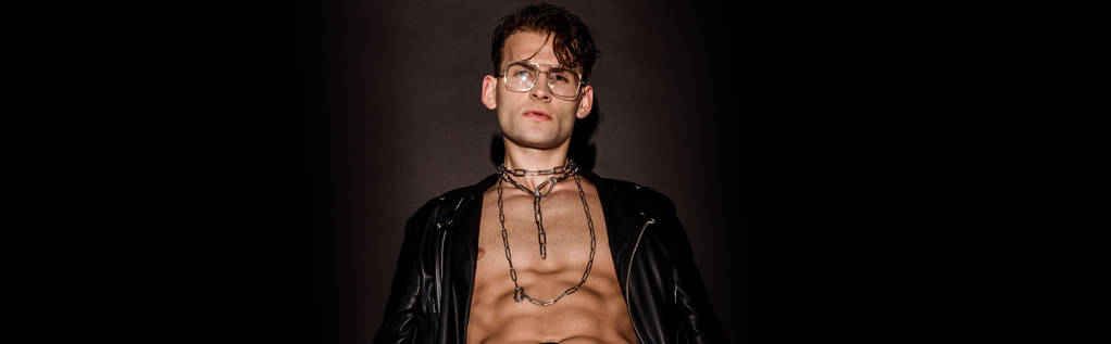 panoramic shot of brutal young man in glasses and leather jacket on black  - Photo, Image
