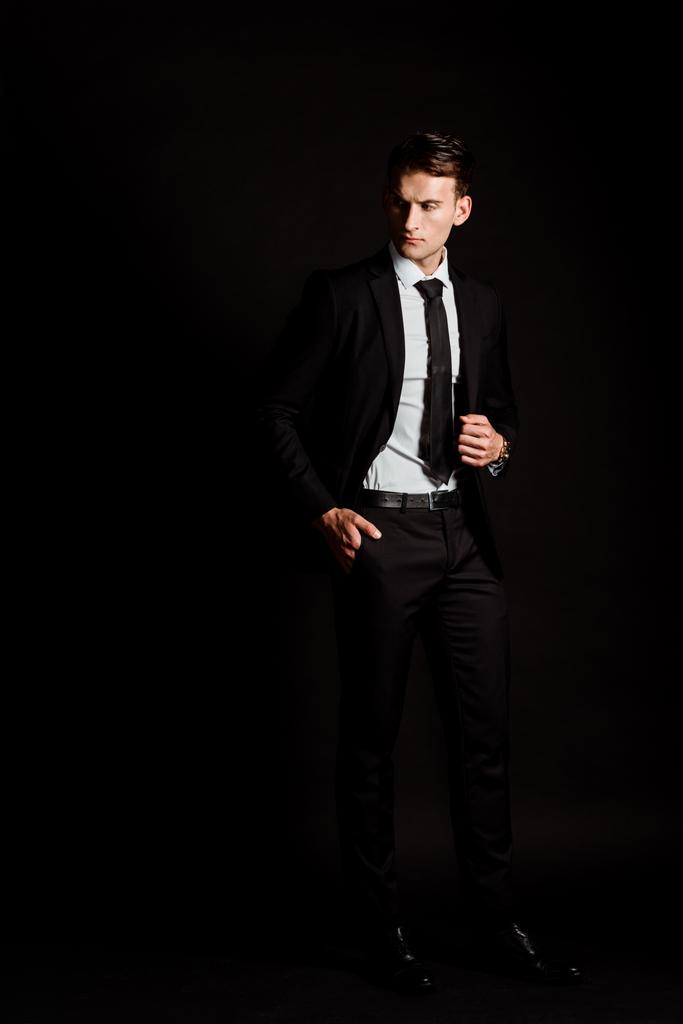 Красивый бизнесмен в костюме стоит с карманом на черном
  - Фото, изображение