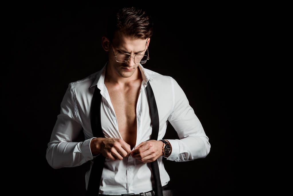 handsome businessman in glasses and formal wear undressing isolated on black  - Photo, Image