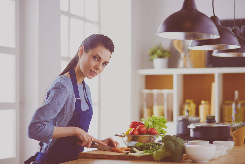 Молодая женщина режет овощи на кухне дома - Фото, изображение