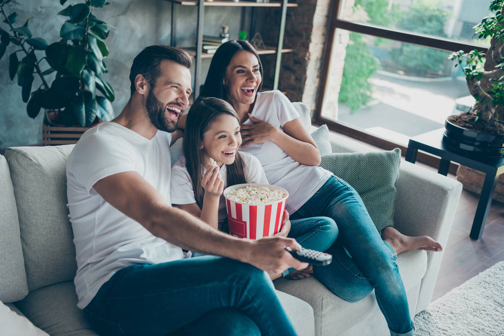 Portret ładne atrakcyjne piękny pozytywny zadowolony wesoły rodzina ubrany casual biały t-shirty dżinsy denim siedzi na Divan zabawy oglądania wideo przełączanie kanału wydatków wolnego czasu - Zdjęcie, obraz