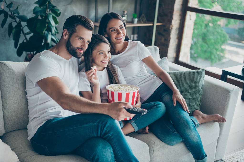 Πορτρέτο της ωραία ελκυστική όμορφη γοητευτική χαρούμενη χαρούμενο οικογένεια φορώντας casual λευκό t-shirt τζιν ντένιμ κάθεται στο ντιβάνι έχοντας τη διασκέδαση βλέποντας σειρά σειριακή βίντεο Εναλλαγή κανάλι σε εσωτερικούς χώρους - Φωτογραφία, εικόνα