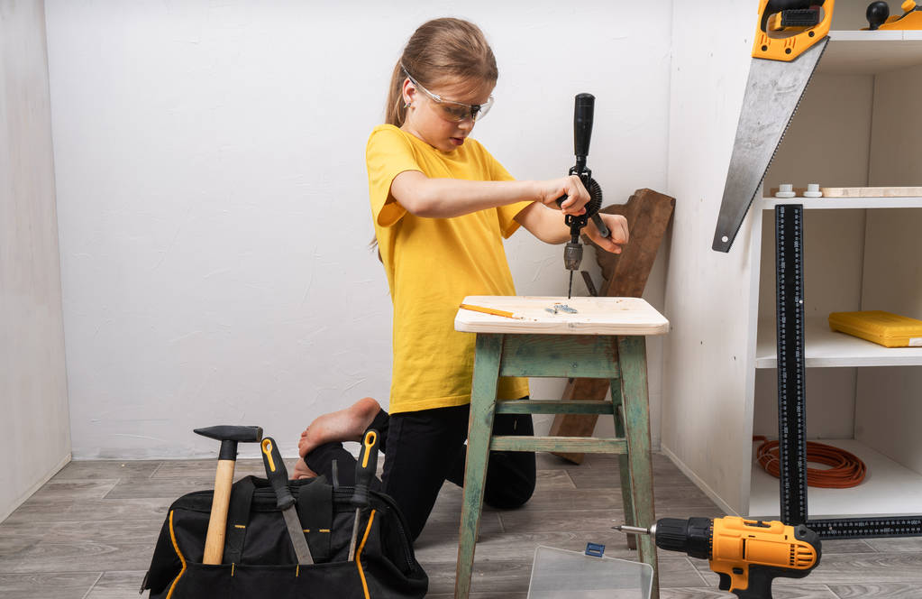 Девушка работает с ручной дрелью и ремонтирует старую мебель
. - Фото, изображение